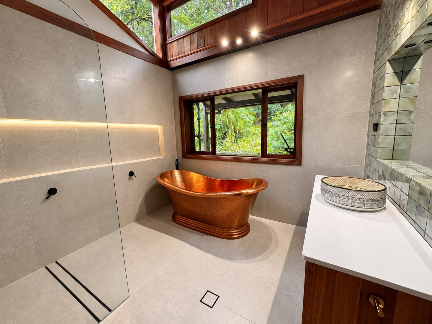 A bathroom with a freestanding copper bath, large format tiles and cedar window frames