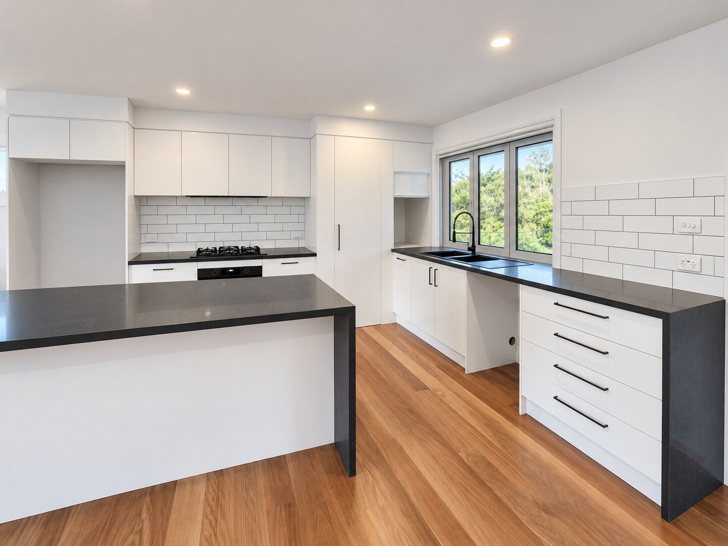 A kitchen with white cabinetry, stone benchtops and blackbutt timber flooring