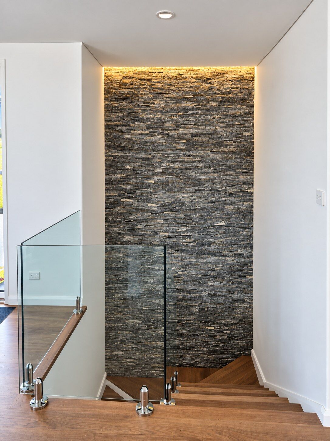 A stacked stone feature wall with concealed LED lighting and a glass balustrade