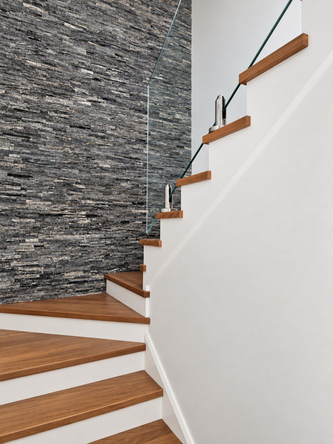 A solid timber staircase with a glass balustrade beside a stacked stone wall